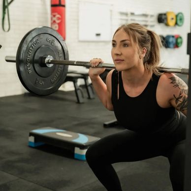 A woman lifting a barbell in a gym, focused and determined.