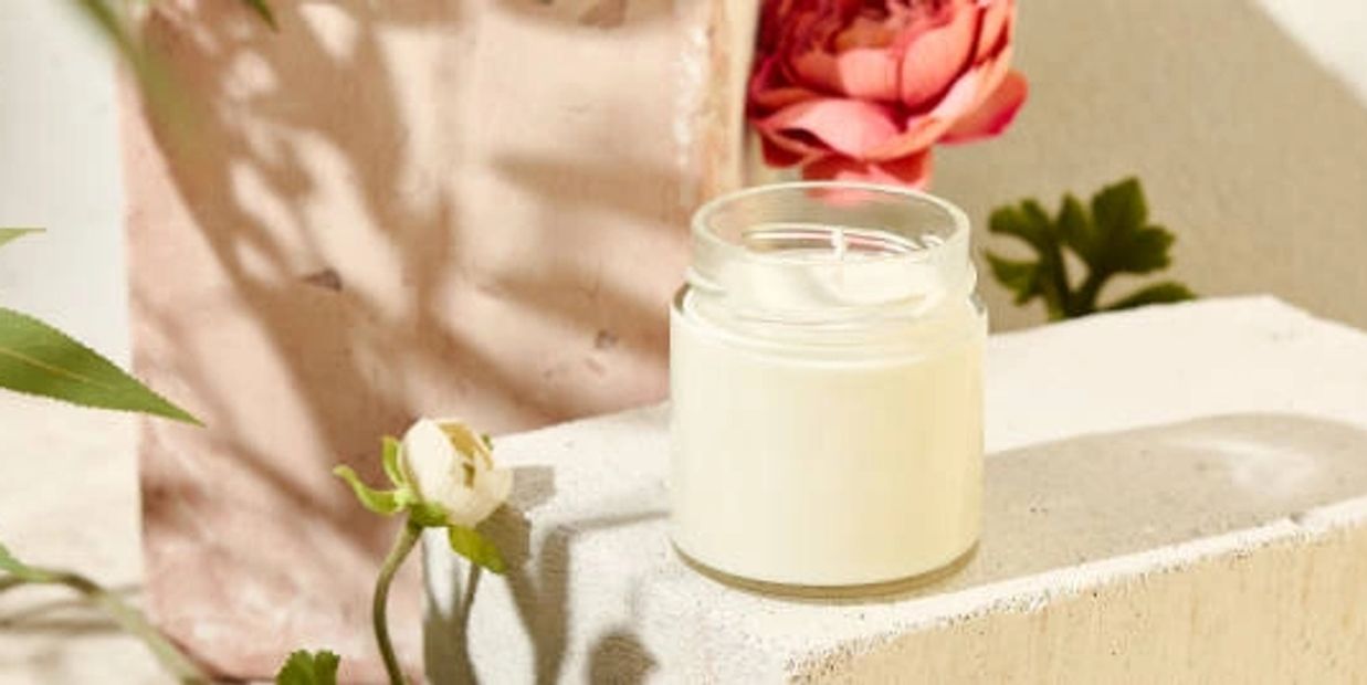 Bougie dans un pot devant un décor de rose et de blanche.