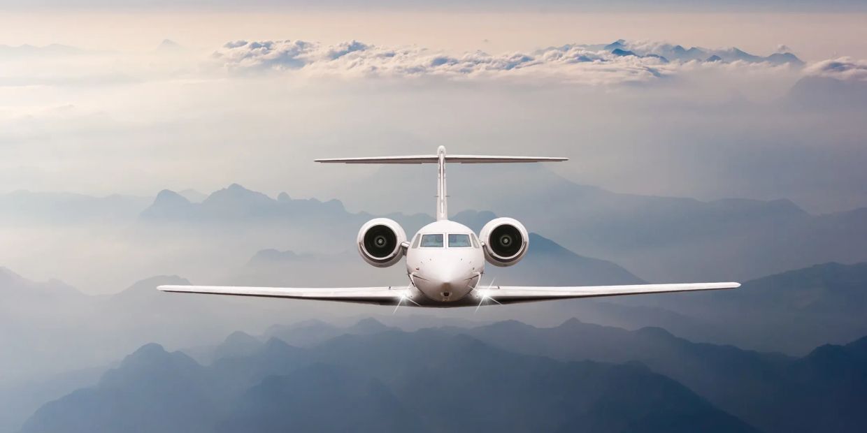 Private jet flying over misty mountains.