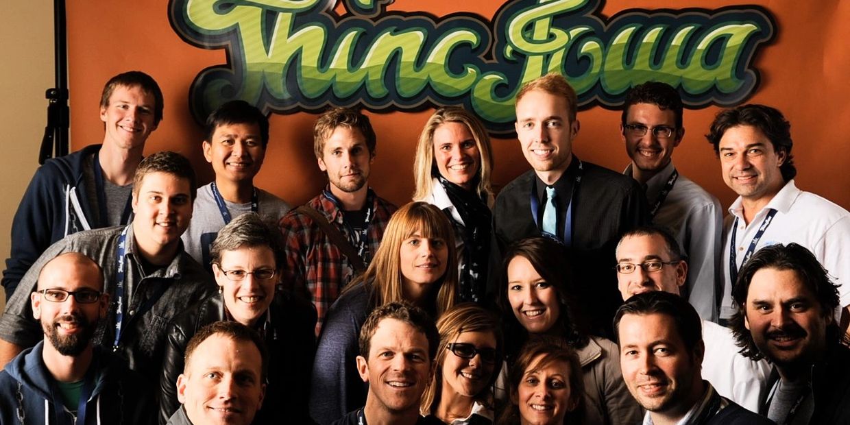 A diverse group of professional colleagues smiling together in front of a green "Thinc Iowa" graffit