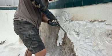 Man using a power tool to remove material from an empty pool wall.