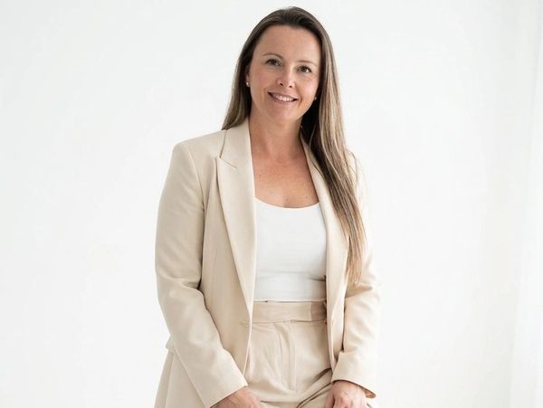 Confident woman in beige suit smiling against a white background.