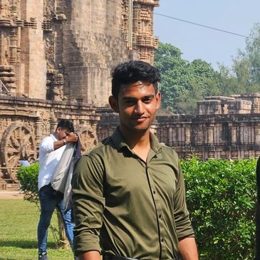 A young man in a green shirt poses in front of an ancient stone temple.