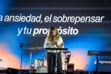 Woman speaking on stage with a motivational message projected behind her.