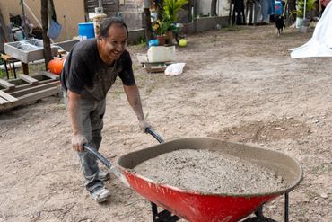 A man pushing a red wheelbarrow filled with cement outdoors.