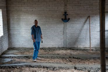Man standing inside a partially constructed building with brick walls and concrete floor.