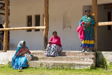 Three women in colorful traditional dresses outside a rustic building.