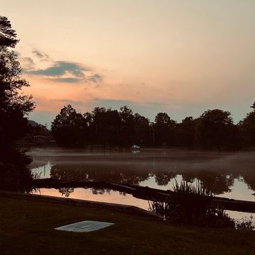 Tranquil sunset over a misty lake surrounded by trees.