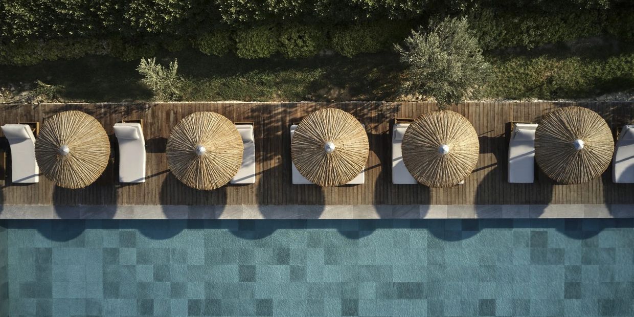 Aerial view of poolside loungers with straw umbrellas and greenery.