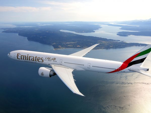 Emirates airplane flying over a scenic coastline with water and islands.