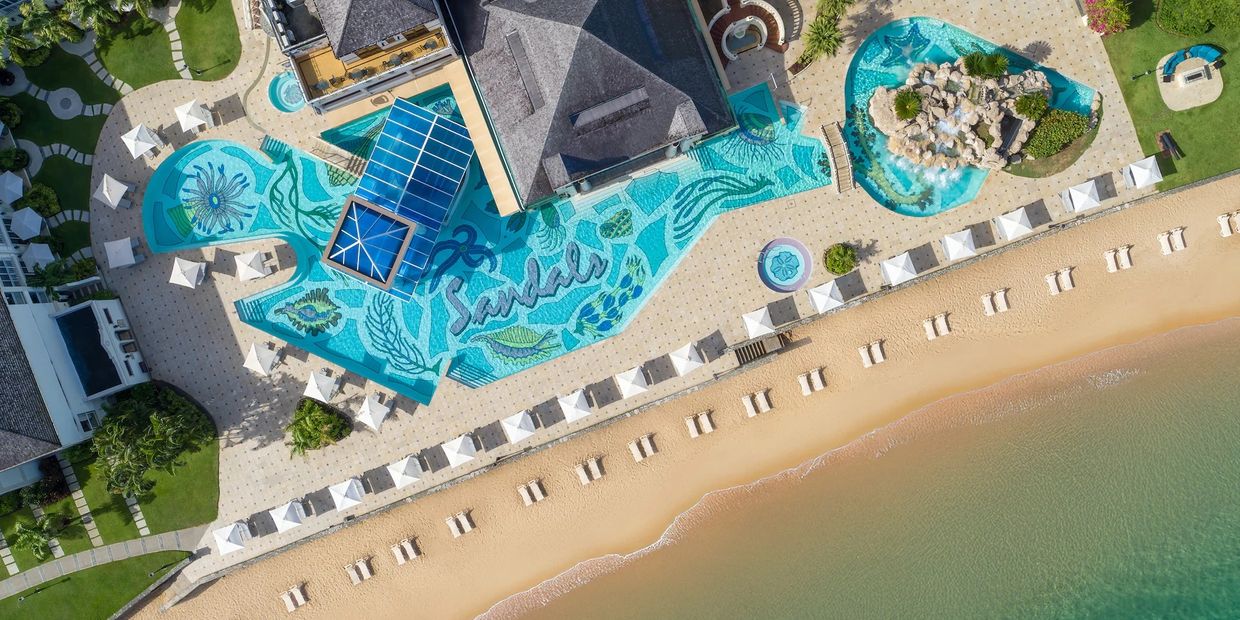 Aerial view of a beach resort with a decorated pool and sun loungers along the sandy shore.