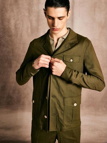 Man buttoning an olive green jacket against a neutral background.