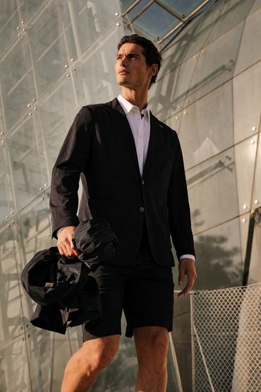 Man in a black blazer and shorts standing confidently outdoors.