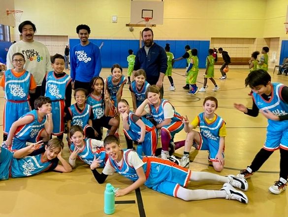 Youth basketball team posing happily in gym with coaches and players in action in background.