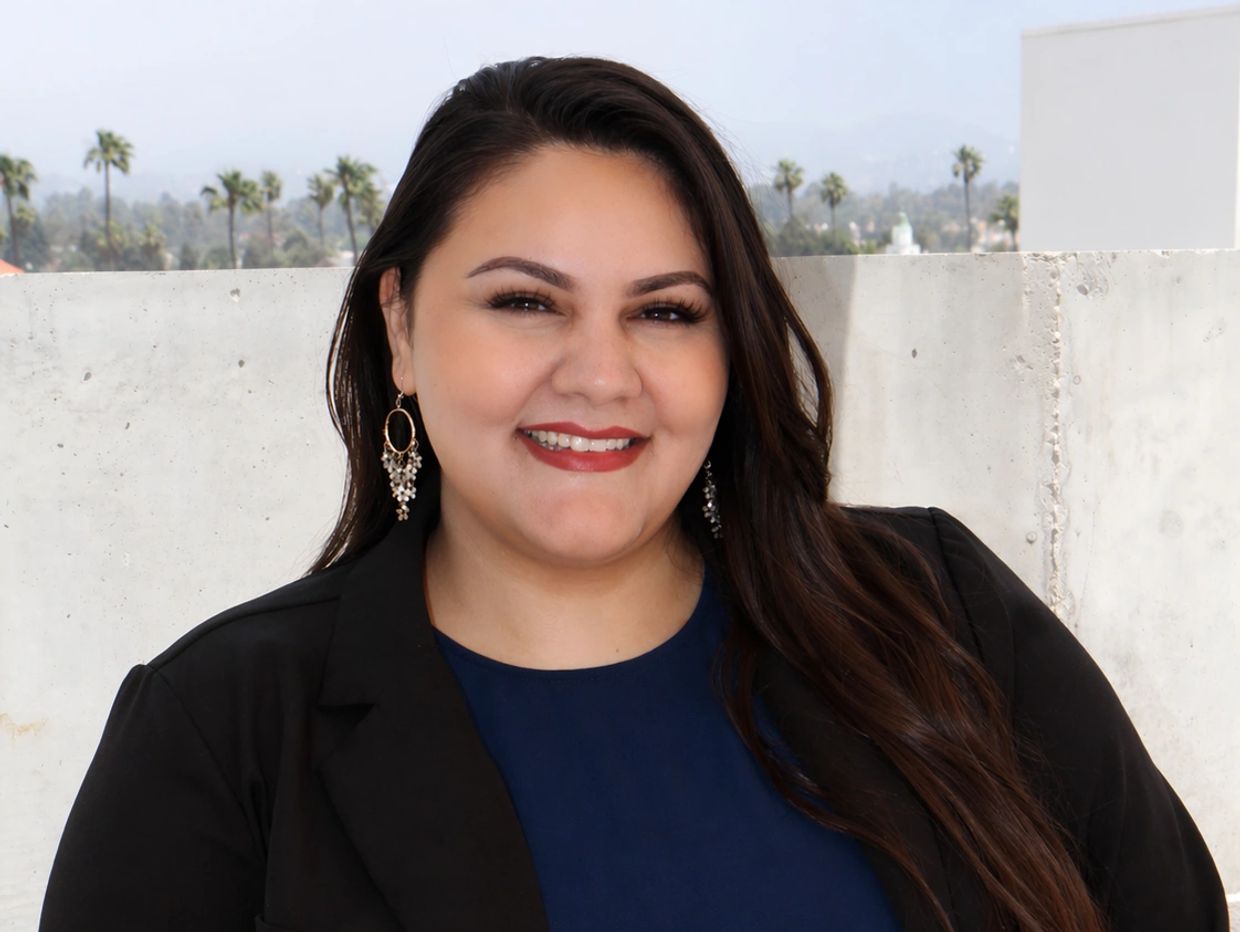 Smiling woman with long hair and earrings outdoors.