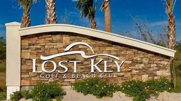 Stone sign for Lost Key Golf &amp; Beach Club with palm trees behind.