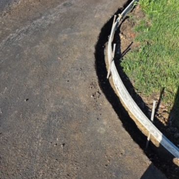 Paved pathway curving next to grass and wooden formwork.