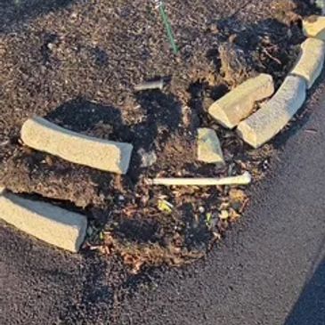 Broken concrete pieces arranged on dirt beside road.