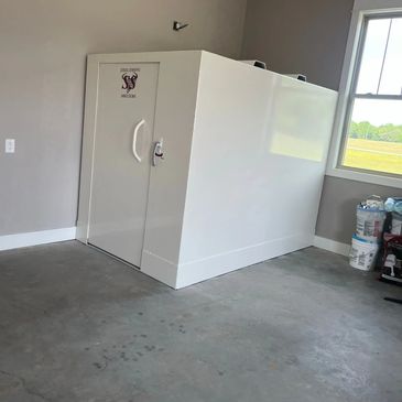 A white steel shelter installed in a room with concrete floor and gray walls.