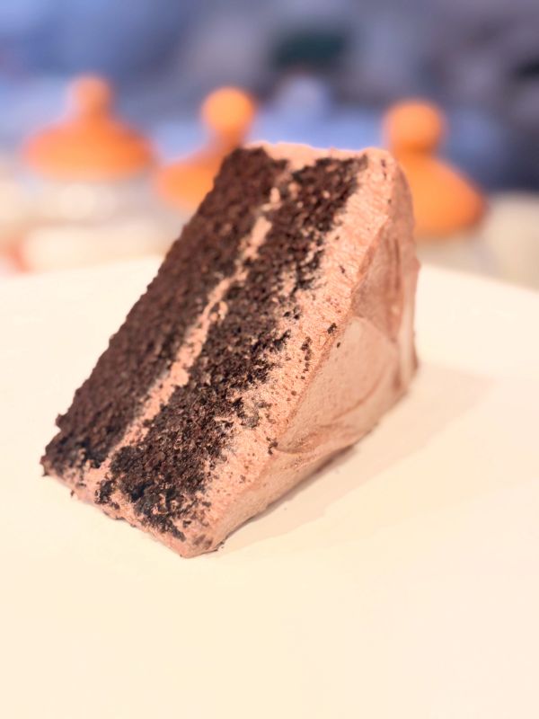 Slice of rich chocolate cake with creamy frosting on a white plate.