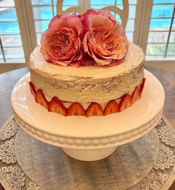 Elegant cake with strawberries and two large pink roses on top.