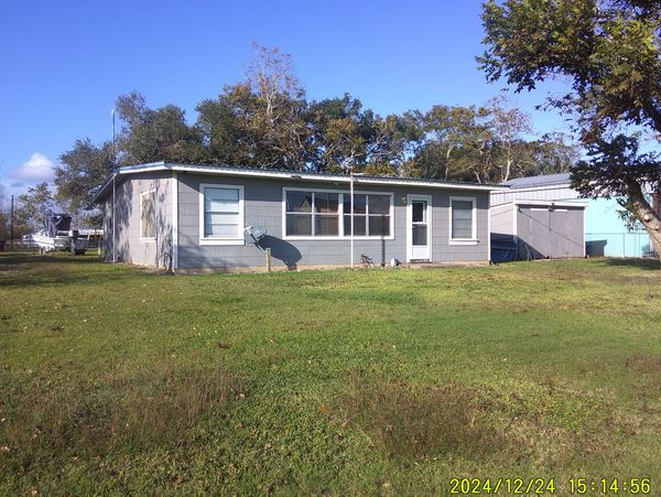 Single-story gray house with a large grassy yard under a clear blue sky.