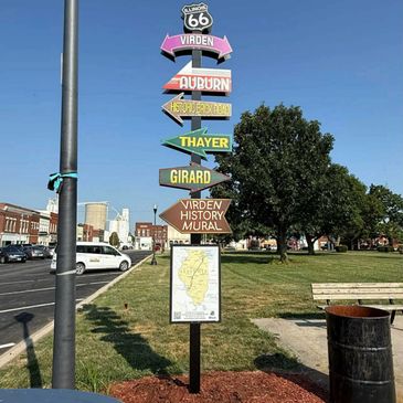Colorful signpost with directional arrows and a Route 66 shield in a park.