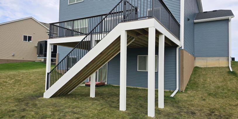 Backyard wooden deck stairs with white supports and black railing.