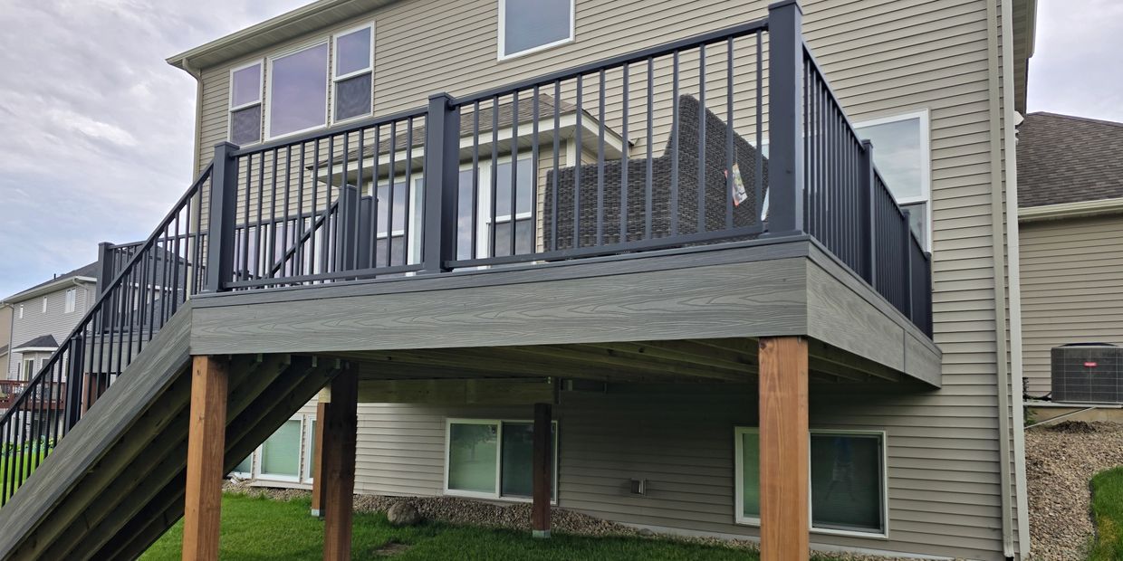 Raised wooden deck with black railing attached to a beige house.