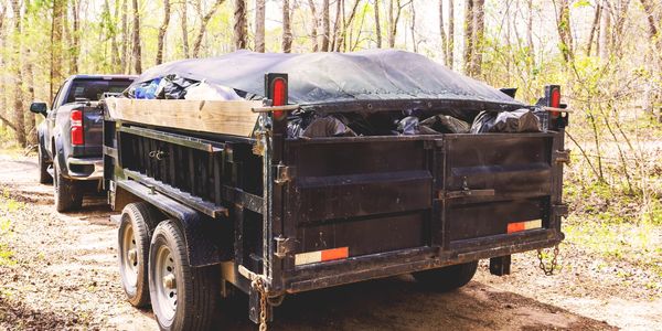 Pickup truck towing a covered dump trailer in a wooded area.