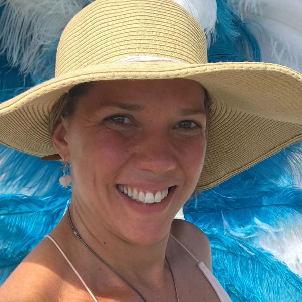 Smiling woman wearing a wide-brimmed hat with blue and white feathers in the background.