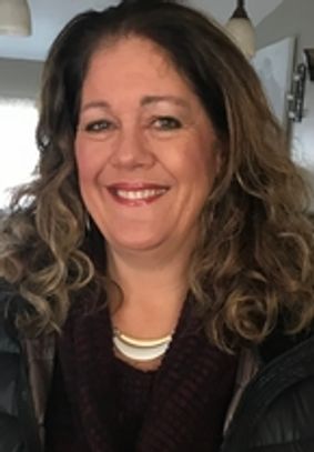 Smiling woman with wavy hair and a warm scarf indoors.