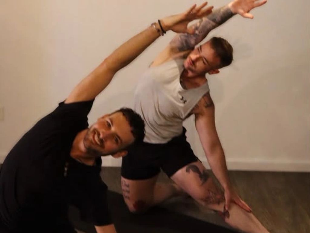 Two men stretching side by side indoors.