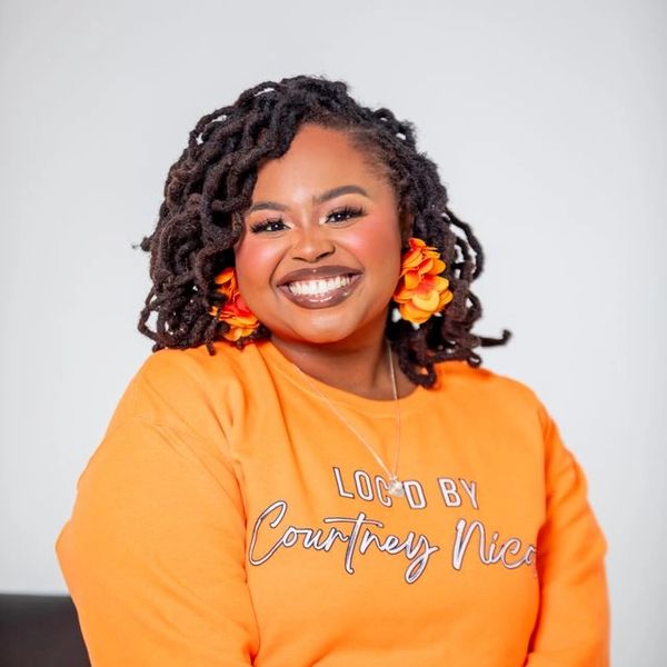Smiling woman with curly hair wearing an orange shirt and flower earrings.