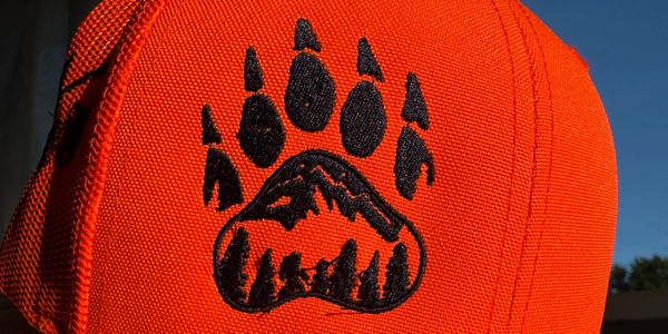 Bright orange cap with black bear paw and mountain design.