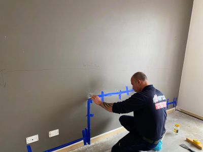 Person applying blue painter's tape for wall preparation.