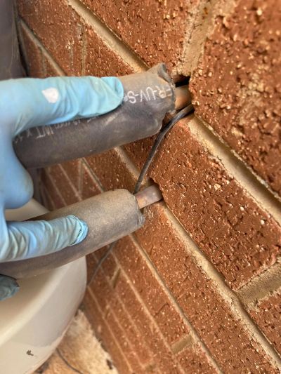 Hand in glove holding insulated wires near a brick wall.