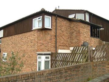 Brick residential building with wooden upper section and fenced yard.