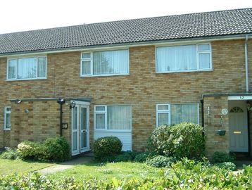 A row of brick terraced houses with green lawns and bushes.