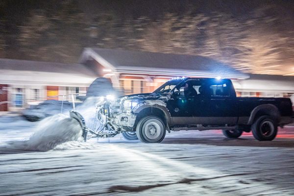 Snowplow truck clearing snow on a street at night.