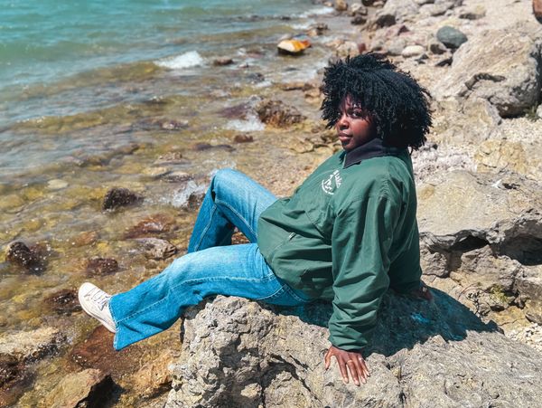 Person relaxing on rocky shore by clear blue water.