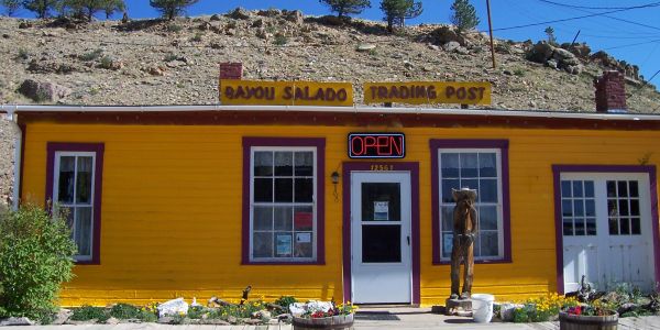 Bright yellow trading post with a wooden sculpture out front.