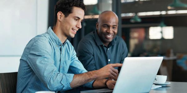 Two men collaborating and smiling while working on a laptop.