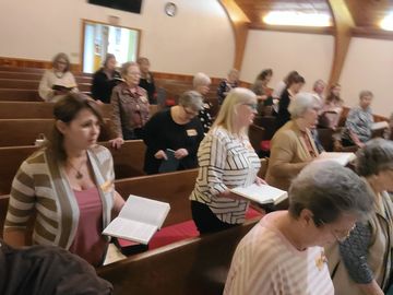 People gathered in pews holding books, likely in a church setting.