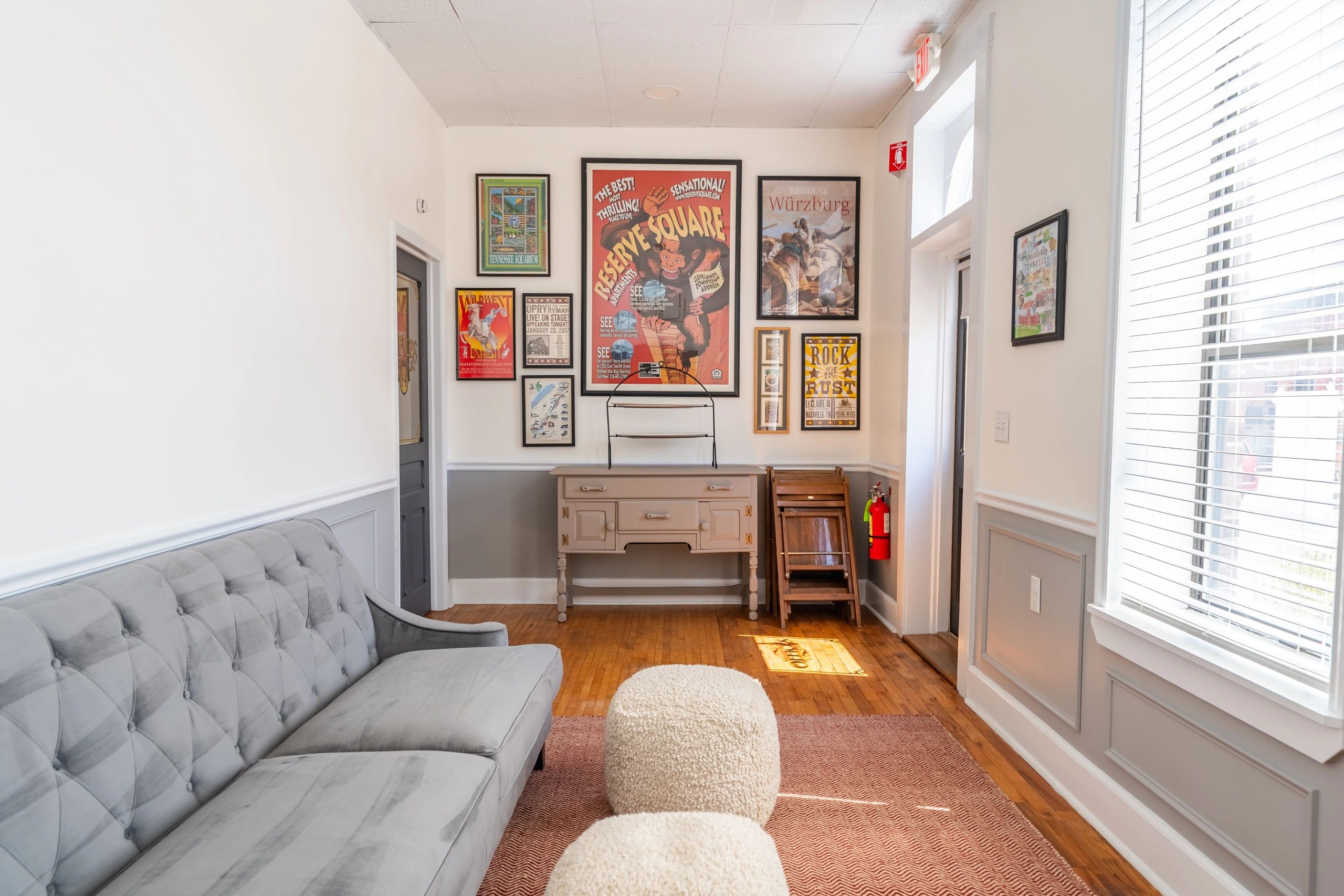 Cozy living room with gray sofa, vintage posters, and soft ottomans.