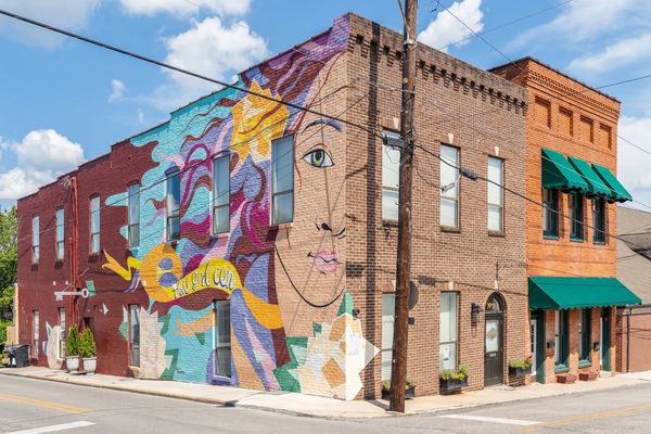 Colorful mural of a woman's face on a brick building at a street corner.