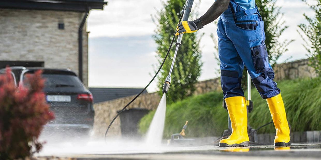 Person pressure washing an outdoor surface wearing yellow boots and blue pants.