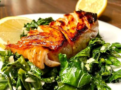 Grilled salmon fillet on a bed of fresh spinach with lemon wedges.
