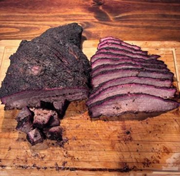 Sliced smoked brisket with a dark crust on a wooden board.