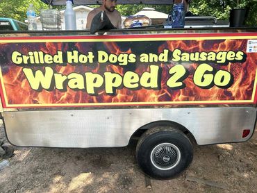 Food cart selling grilled hot dogs and sausages to go with a fiery sign.